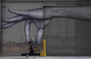 TIMOTHY A. CLARY/AFP | Une femme masquée passe devant ce graffiti peint dans un mur à New York, en une image du 22 avril 2020 présent à l'exposition <em>Pandèmie(s)</em>