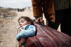 OMAR SANADIKI/UNOCHA | Un niño es transportado dentro de una maleta durante la evacuación de Beit Sawa, en la Guta, al este de Damasco, en marzo de 2018, después de la derrota de los rebeldes contra el régimen de Bashar al-Ásad